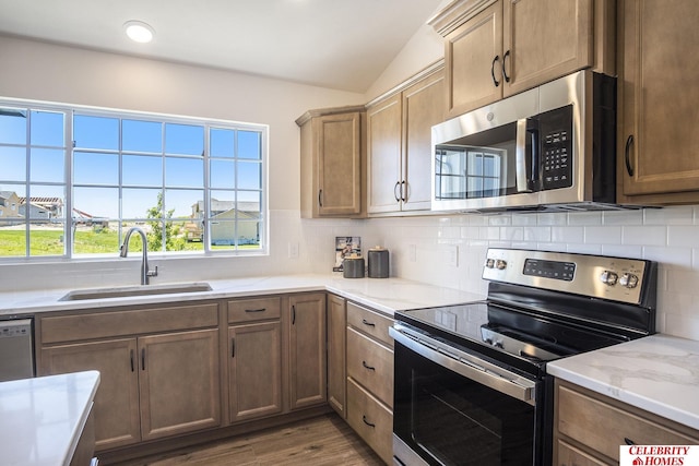 kitchen with appliances with stainless steel finishes, light wood-type flooring, backsplash, vaulted ceiling, and sink