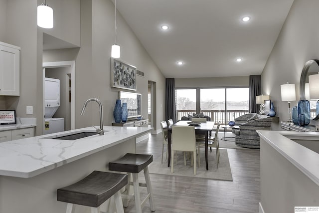 kitchen featuring sink, light hardwood / wood-style flooring, decorative light fixtures, white cabinetry, and stacked washer / dryer