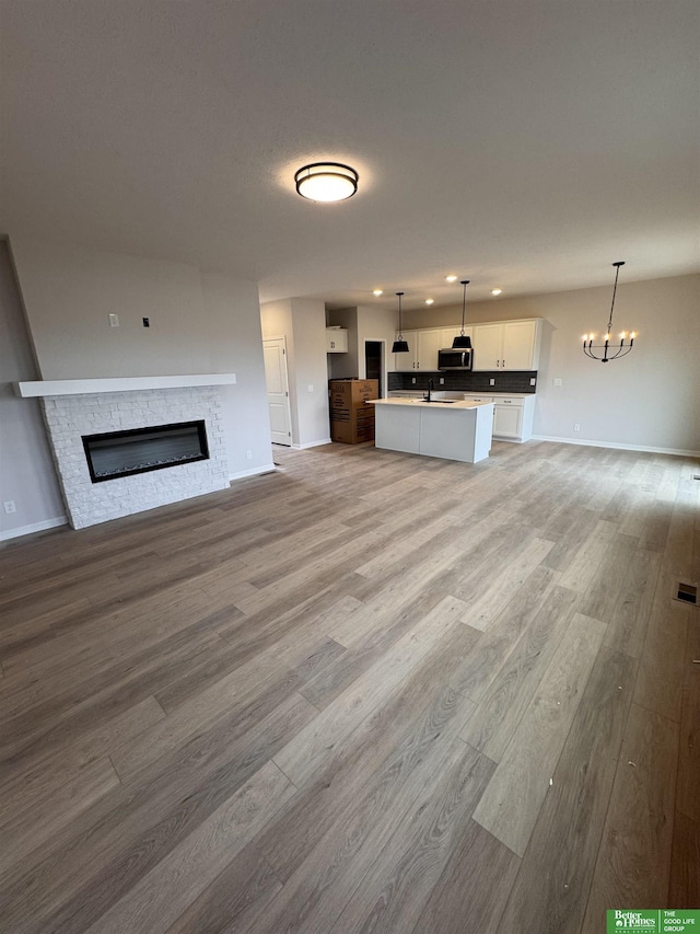 unfurnished living room featuring a stone fireplace, light wood-type flooring, sink, and an inviting chandelier