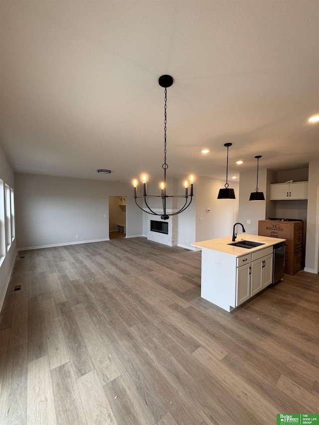 kitchen with a kitchen island with sink, sink, decorative light fixtures, light hardwood / wood-style flooring, and white cabinetry