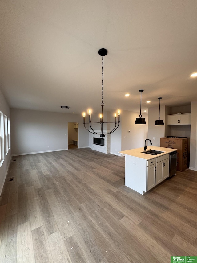 kitchen featuring sink, decorative light fixtures, a center island with sink, light hardwood / wood-style floors, and white cabinetry