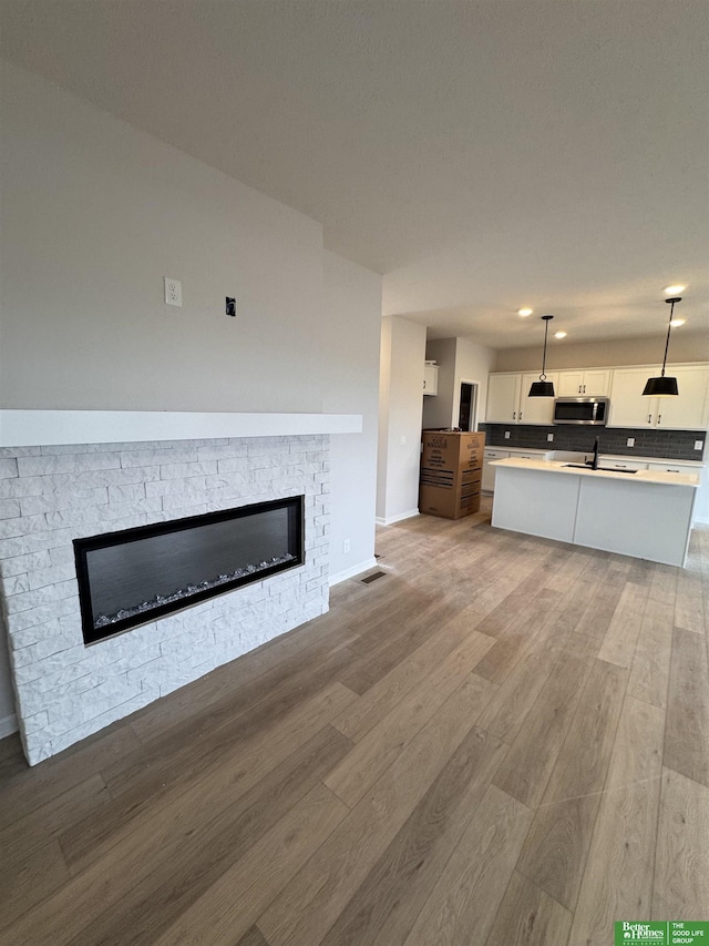 unfurnished living room with light wood-type flooring, a stone fireplace, and sink