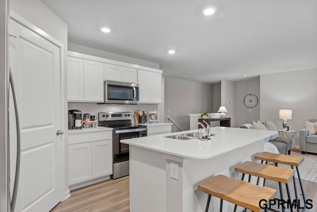 kitchen with white cabinetry, sink, stainless steel appliances, a breakfast bar area, and a center island with sink