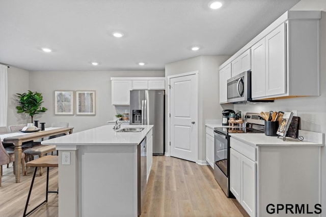 kitchen with stainless steel appliances, a center island with sink, light hardwood / wood-style flooring, white cabinetry, and a breakfast bar area