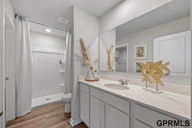 bathroom with hardwood / wood-style floors, vanity, toilet, and walk in shower