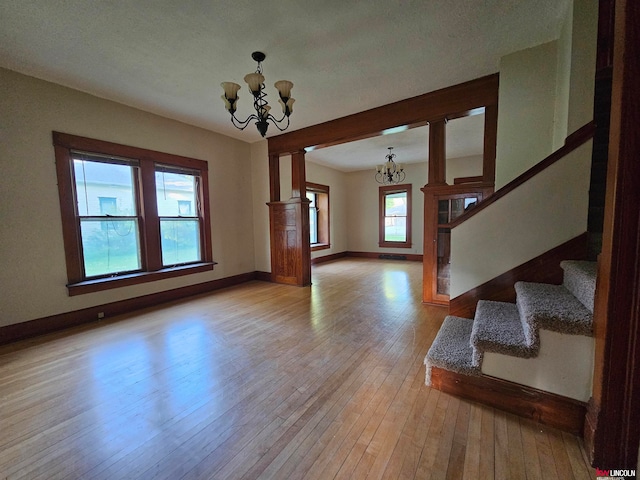 foyer entrance with a textured ceiling, a notable chandelier, hardwood / wood-style floors, and decorative columns