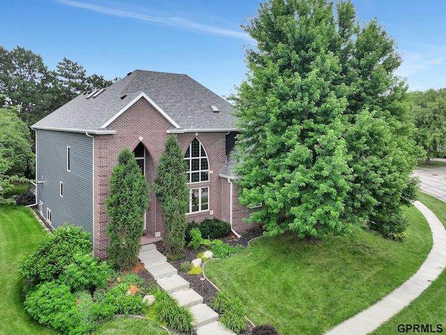 view of front of house with a front yard, roof with shingles, and brick siding