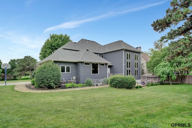 back of property featuring a shingled roof, a yard, and fence