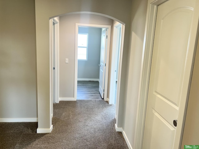 corridor featuring arched walkways, dark carpet, and baseboards