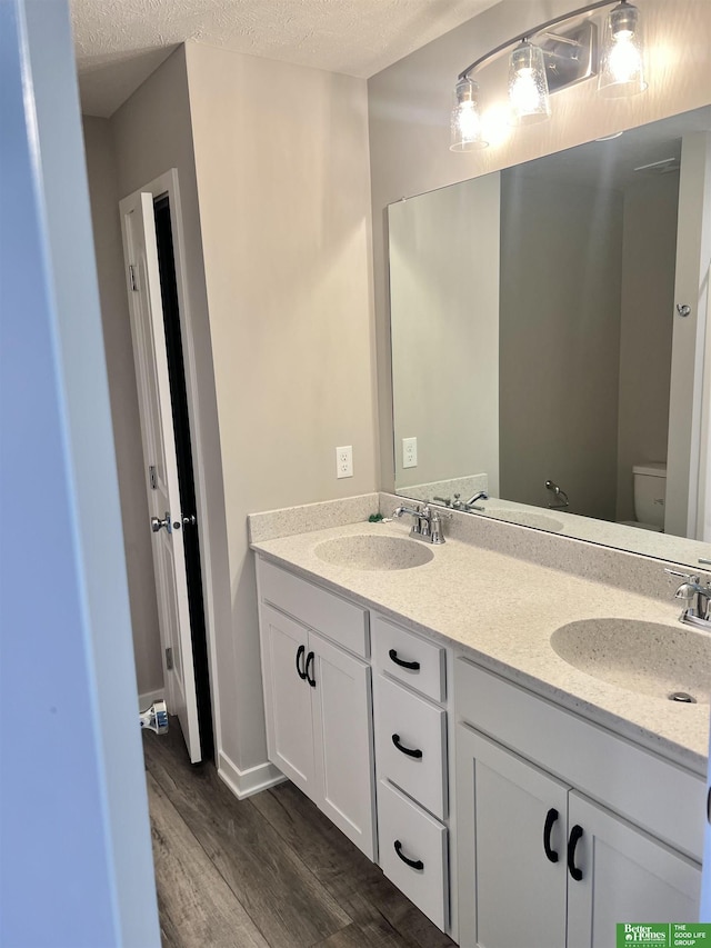 bathroom with wood finished floors, toilet, double vanity, and a textured ceiling