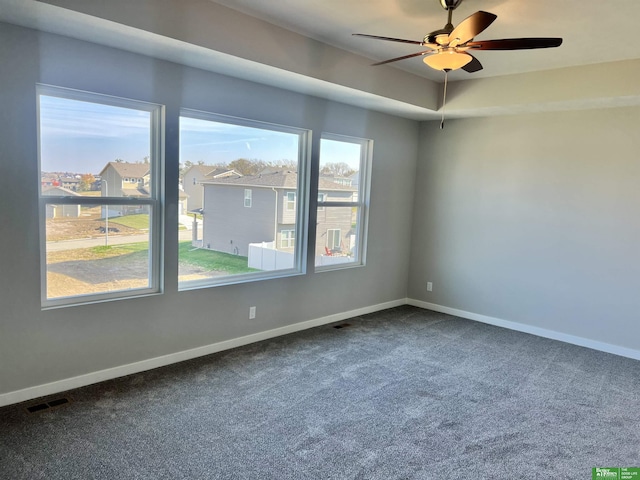 empty room with dark carpet, a ceiling fan, and baseboards