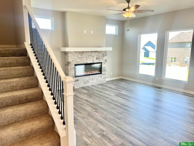 unfurnished living room with a stone fireplace, ceiling fan, and hardwood / wood-style flooring