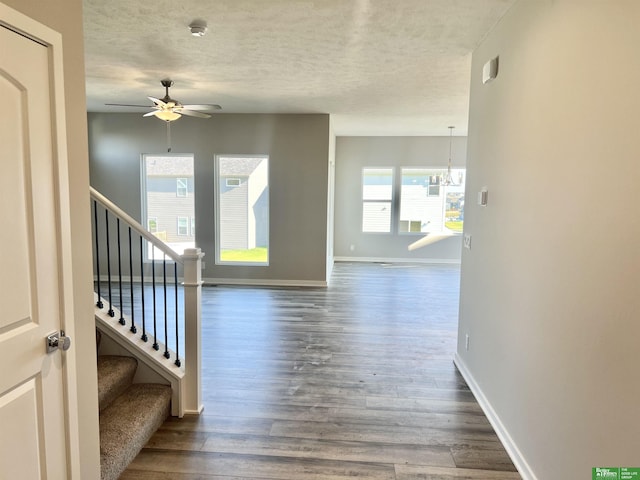 hallway with a textured ceiling, dark wood-type flooring, baseboards, stairs, and a chandelier