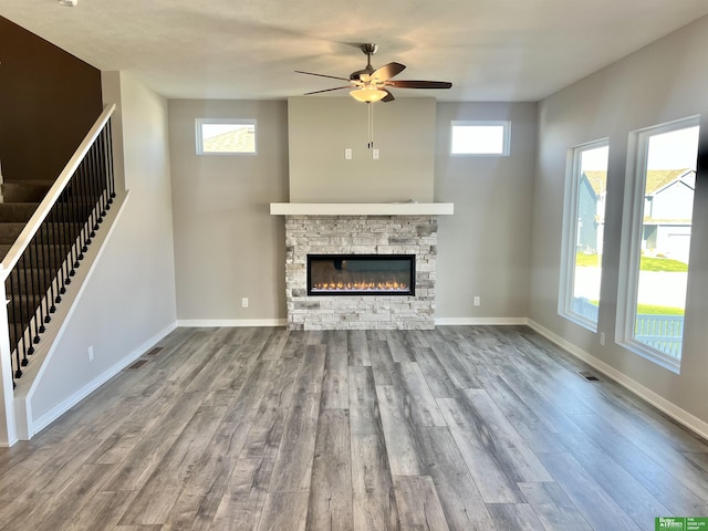 unfurnished living room with stairs, wood finished floors, a ceiling fan, and a stone fireplace