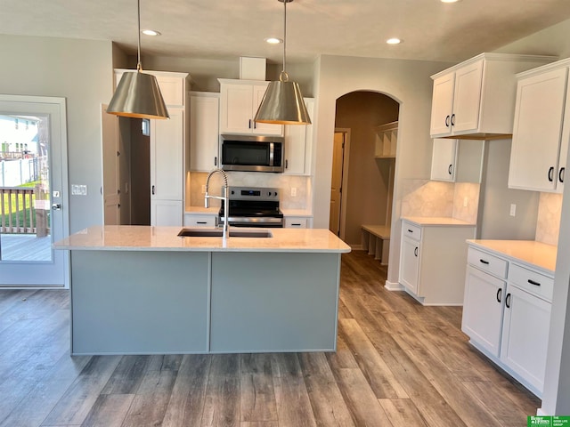 kitchen with white cabinets, decorative light fixtures, a center island with sink, and appliances with stainless steel finishes