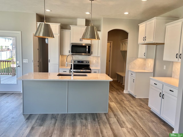 kitchen featuring appliances with stainless steel finishes, a sink, arched walkways, backsplash, and recessed lighting