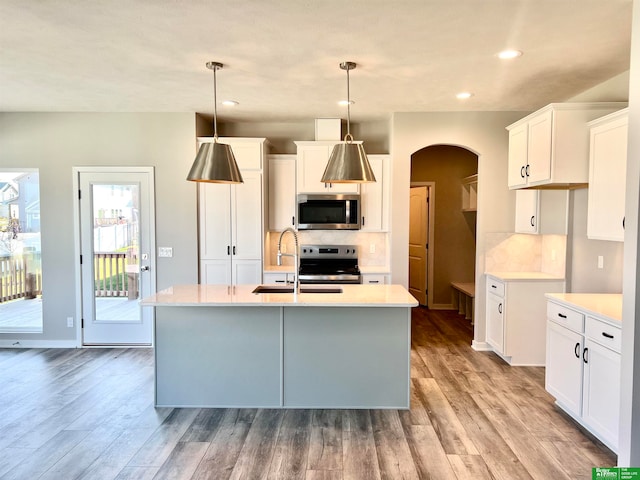 kitchen featuring white cabinets, decorative light fixtures, stainless steel appliances, and a center island with sink