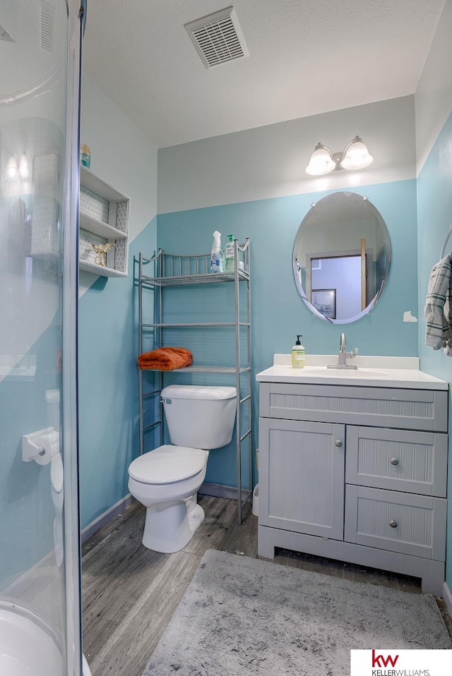 bathroom featuring wood-type flooring, walk in shower, vanity, and toilet