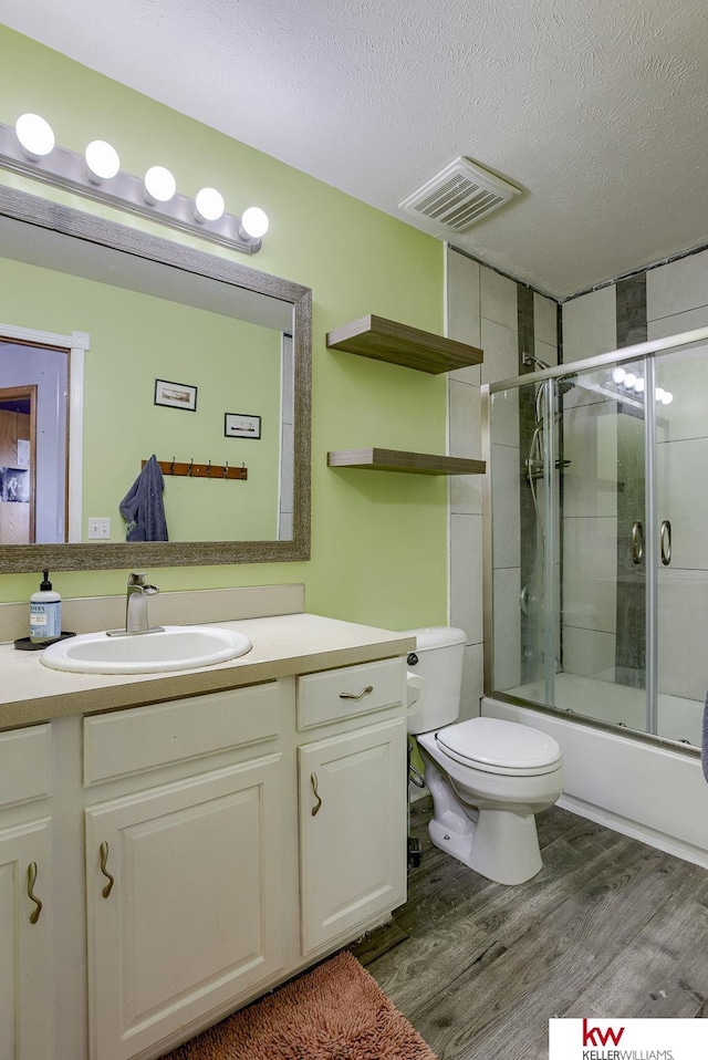 full bathroom featuring vanity, a textured ceiling, combined bath / shower with glass door, hardwood / wood-style flooring, and toilet