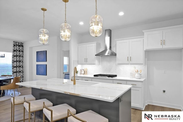 kitchen with light hardwood / wood-style floors, an island with sink, pendant lighting, backsplash, and wall chimney exhaust hood