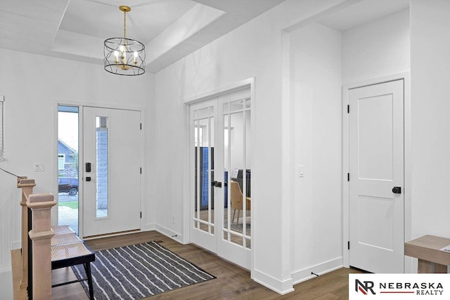 entryway with an inviting chandelier, hardwood / wood-style floors, and a tray ceiling