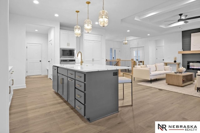 kitchen featuring light hardwood / wood-style flooring, an island with sink, pendant lighting, white cabinetry, and appliances with stainless steel finishes