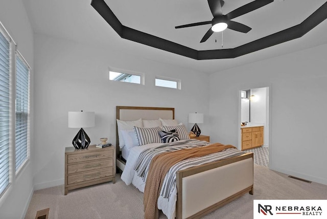 bedroom featuring light colored carpet, ensuite bath, ceiling fan, and a raised ceiling