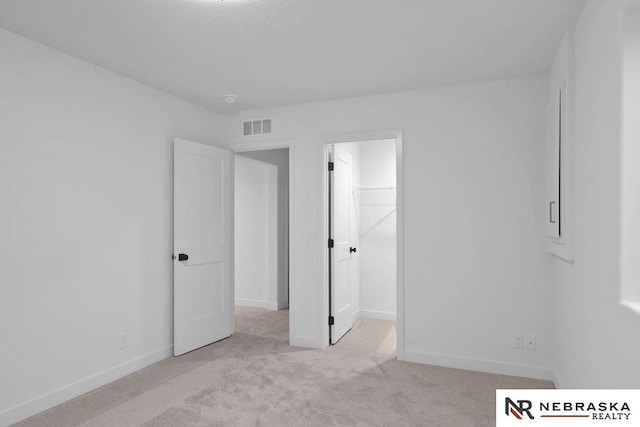 unfurnished bedroom with a spacious closet, a closet, and light colored carpet