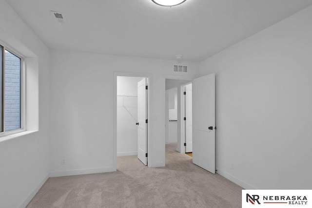 unfurnished bedroom featuring light carpet, a walk in closet, and a closet