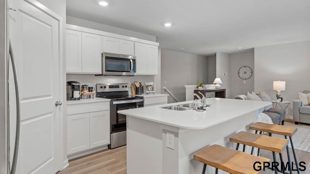 kitchen with white cabinetry, stainless steel appliances, a kitchen breakfast bar, and a center island with sink