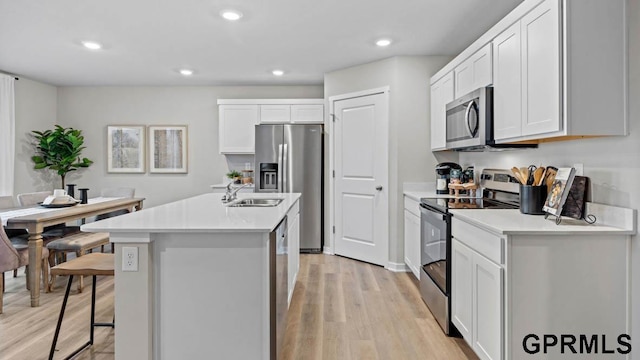 kitchen with sink, light hardwood / wood-style flooring, white cabinetry, stainless steel appliances, and a center island with sink