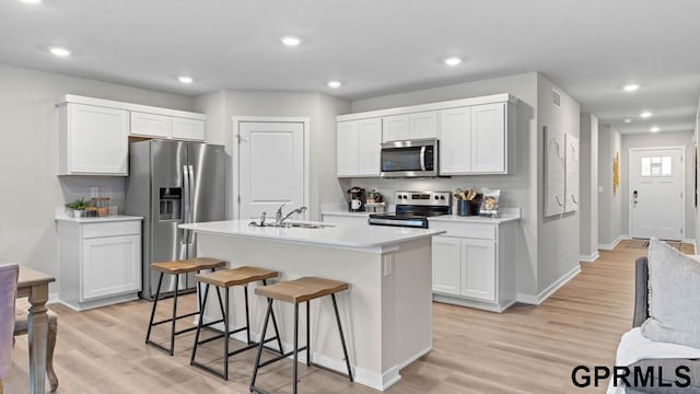 kitchen with white cabinetry, appliances with stainless steel finishes, light hardwood / wood-style floors, and an island with sink