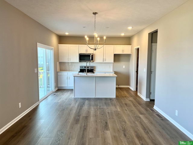 kitchen with stainless steel appliances, white cabinets, pendant lighting, backsplash, and a kitchen island with sink