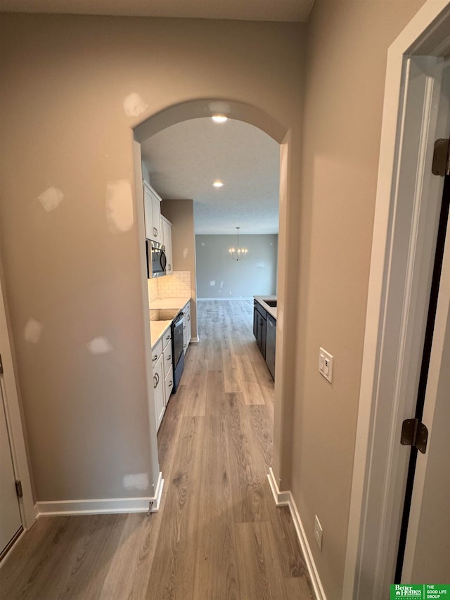 hall with light wood-type flooring and a notable chandelier