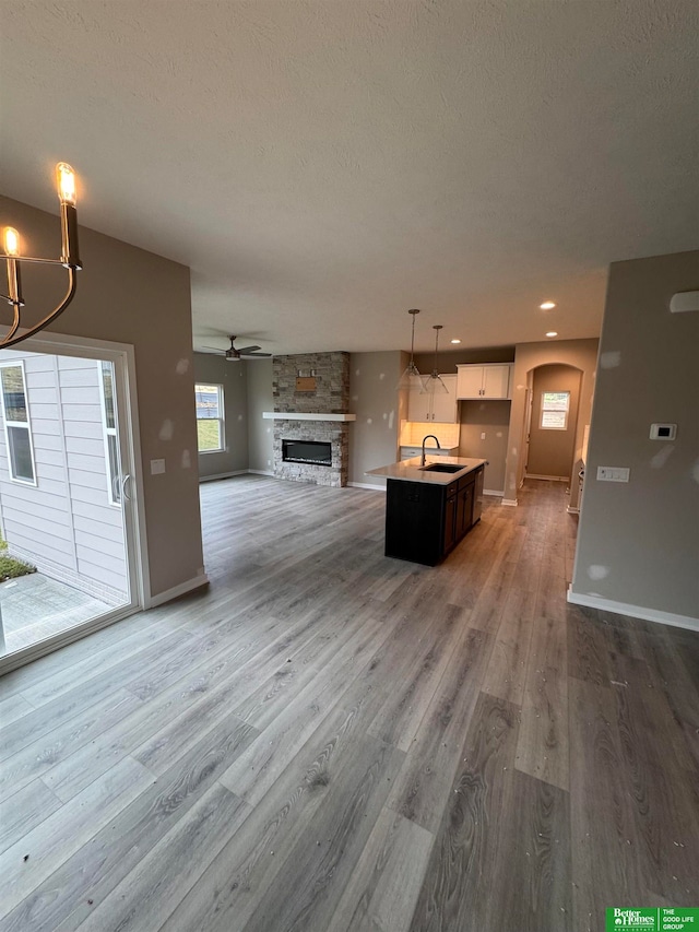 unfurnished living room with ceiling fan with notable chandelier, sink, hardwood / wood-style flooring, a fireplace, and a textured ceiling