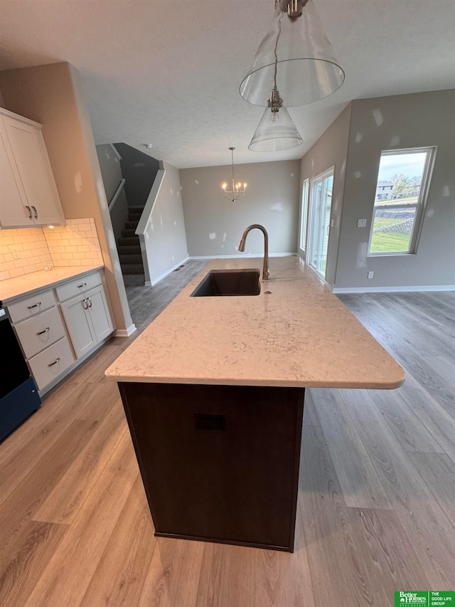 kitchen with pendant lighting, a center island with sink, sink, decorative backsplash, and white cabinetry