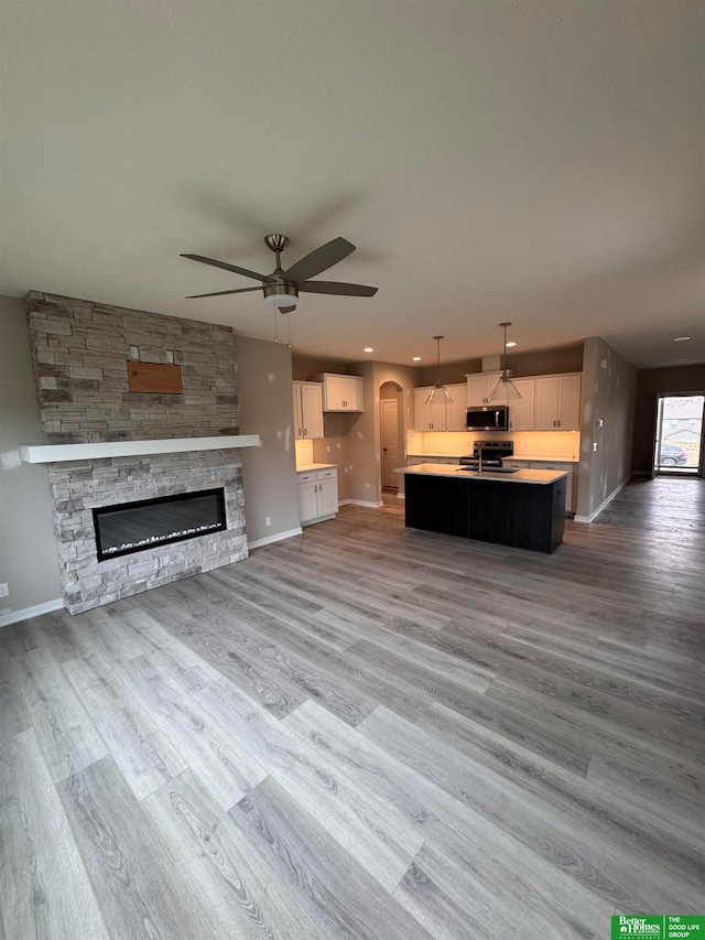 unfurnished living room with light wood-type flooring, a stone fireplace, and ceiling fan