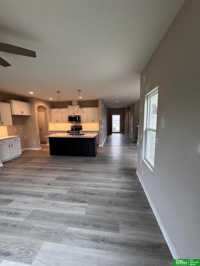 kitchen with light hardwood / wood-style flooring, decorative light fixtures, a kitchen island with sink, white cabinets, and appliances with stainless steel finishes