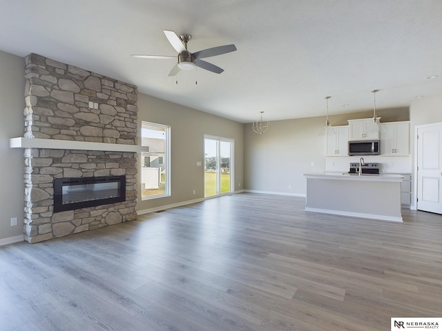 unfurnished living room featuring light hardwood / wood-style floors, a stone fireplace, and ceiling fan