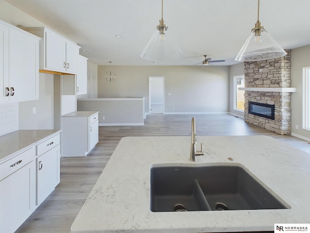 kitchen featuring white cabinetry, sink, ceiling fan, a stone fireplace, and decorative light fixtures