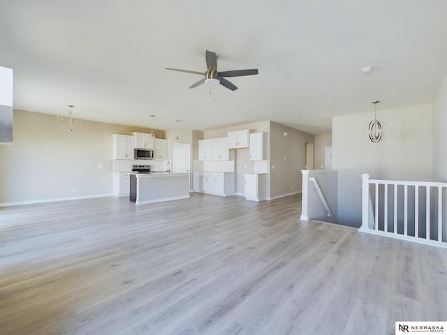 unfurnished living room featuring ceiling fan with notable chandelier, light wood-type flooring, and sink