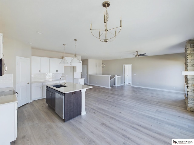 kitchen featuring a kitchen island with sink, hanging light fixtures, sink, stainless steel dishwasher, and white cabinetry