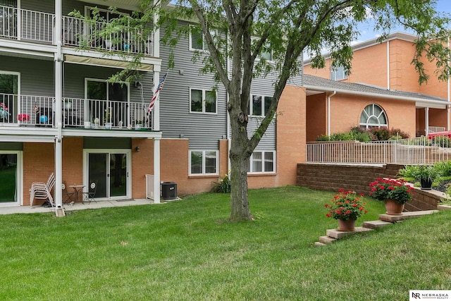 back of property with a balcony, a yard, and central air condition unit