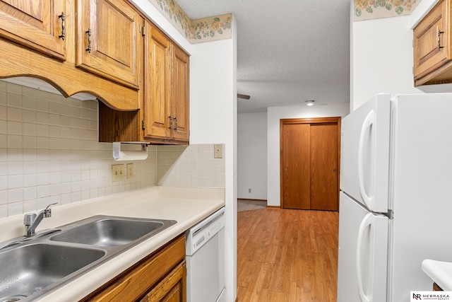 kitchen featuring decorative backsplash, a textured ceiling, white appliances, sink, and light hardwood / wood-style floors