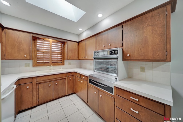 kitchen featuring light tile patterned flooring, sink, tasteful backsplash, and a skylight