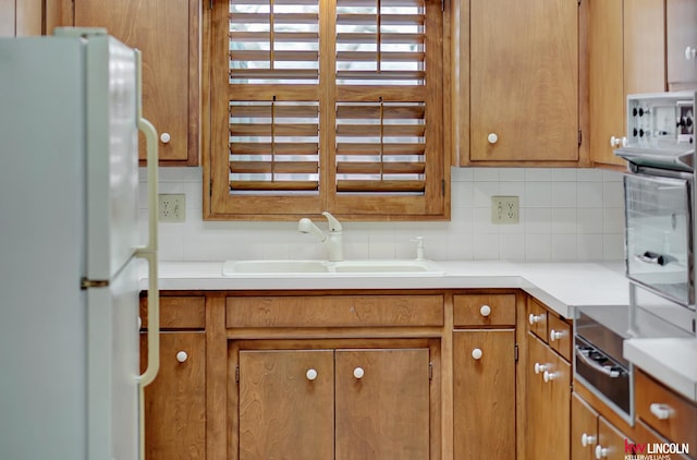 kitchen with cooktop, sink, white refrigerator, and decorative backsplash