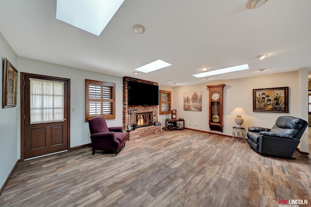 living room with a skylight, a brick fireplace, brick wall, and hardwood / wood-style floors