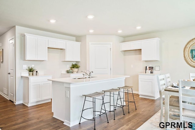 kitchen with hardwood / wood-style flooring, a kitchen island with sink, sink, and white cabinets