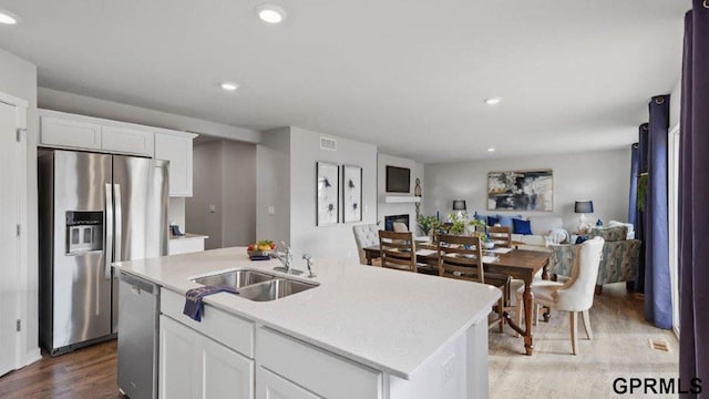 kitchen with sink, white cabinetry, an island with sink, stainless steel appliances, and hardwood / wood-style floors