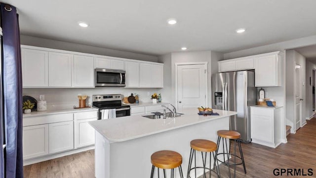 kitchen with hardwood / wood-style floors, white cabinetry, sink, stainless steel appliances, and a center island with sink